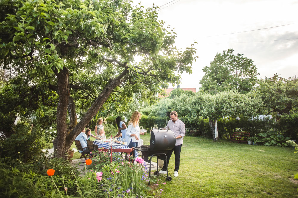 En familj och vänner grillar i en stor trädgård